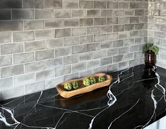 a black counter top with some green vegetables in a wooden bowl on it and a brick wall behind it