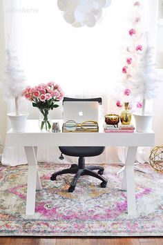 a white desk with flowers on it in front of a window and a laptop computer