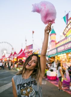 a woman holding up a pink cotton candy in the air at an amusement park,