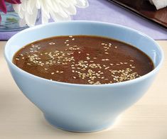 a blue bowl filled with soup sitting on top of a table next to a flower