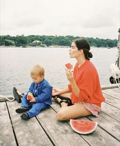 a woman is sitting on the dock eating watermelon and holding a piece of watermelon