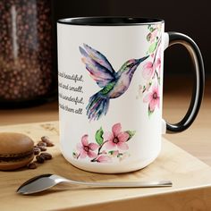 a coffee mug with a hummingbird painted on it and a spoon next to it