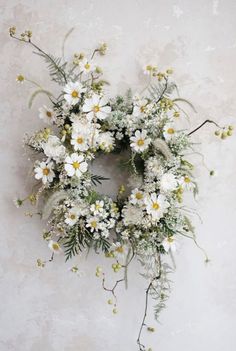 a wreath with white flowers and greenery hanging on a wall in front of a stucco wall