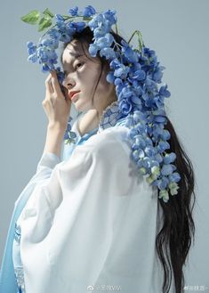 a woman with blue flowers on her head talking on a cell phone while wearing a white dress