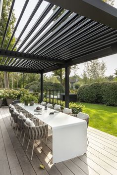 an outdoor dining area with white table and chairs on wooden flooring, surrounded by greenery