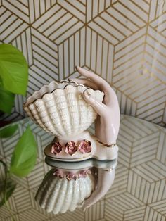 a ceramic figurine holding a seashell on top of a glass table next to a potted plant