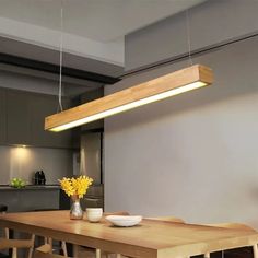 a wooden table sitting under a light fixture in a kitchen next to a bowl of yellow flowers