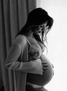 a pregnant woman is standing in front of a window with her hands on her belly