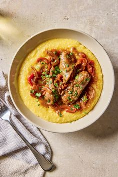 a white bowl filled with meat and vegetables on top of mashed potatoes next to a fork