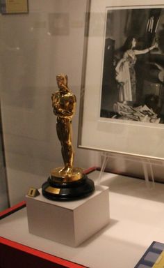 an oscar statue on display in a glass case with a black and white photo behind it