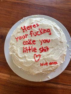 a cake with writing on it sitting on top of a white plate next to a wooden table