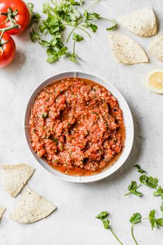 a white bowl filled with salsa surrounded by tortilla chips, tomatoes and cilantro