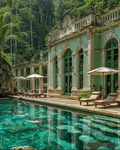 an outdoor swimming pool with chaise lounges and umbrellas next to the building