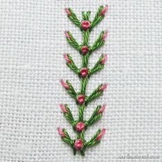 a close up of a piece of embroidery with pink flowers on white fabric and green needles