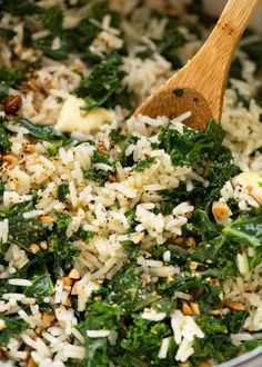 rice and greens are mixed together in a bowl with a wooden spoon on the side