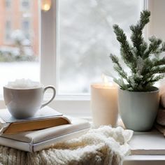 a cup of coffee on a window sill next to a book and a candle