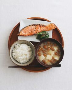 a wooden plate topped with rice, meat and veggies next to chopsticks