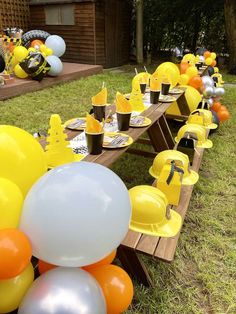 a long table with yellow and orange balloons on it is set up for an outdoor birthday party