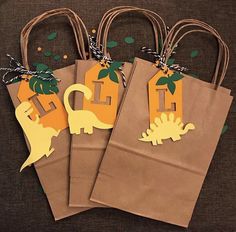 three brown paper bags with dinosaur tags on them, one has a house and the other is a t - rex