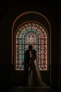 a bride and groom standing in front of a stained glass window