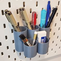 several pens, pencils and markers are placed in cups on a wall mounted organizer