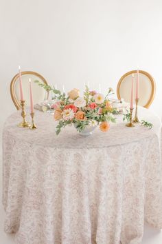 a table with flowers, candles and plates on it in front of a white wall