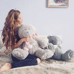 a woman sitting on a bed with two stuffed animals in her lap and holding the teddy bear