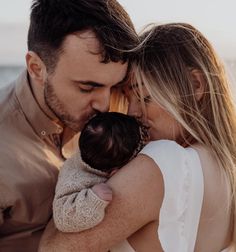 a man and woman holding a baby in their arms while standing next to the ocean