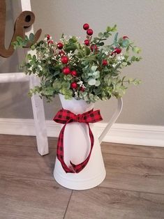 a white vase with red berries and greenery tied around it on a wooden floor