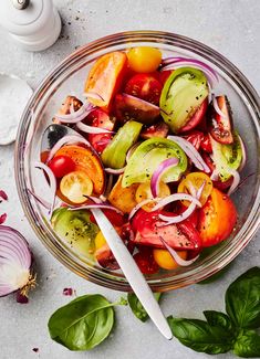 a glass bowl filled with sliced tomatoes, onions and other vegetables next to a spoon