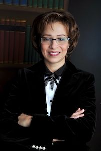 a woman wearing glasses and a bow tie standing in front of a bookshelf