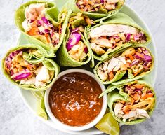 a white plate topped with lettuce wrapped in tortilla wrappers next to a bowl of salsa