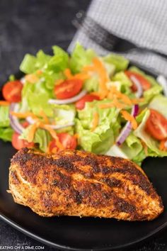 a black plate topped with meat next to a salad