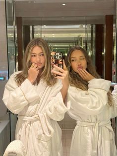 two women in white robes taking selfies with their cell phones