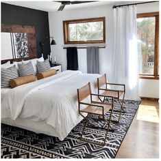 a bed with white sheets and pillows in a bedroom next to two wooden chairs on top of a rug