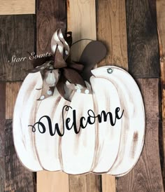 a white pumpkin with the word welcome painted on it and a brown bow is sitting on a wooden floor