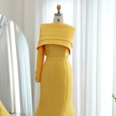 a yellow dress is on display in front of a mirror and a vase with flowers