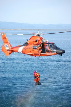 an orange helicopter is being lowered into the water by a man in a life jacket