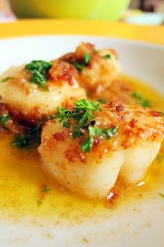 two scallops on a white plate with sauce and parsley in the middle