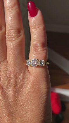 a woman's hand with a three stone ring on top of her finger and red nail polish