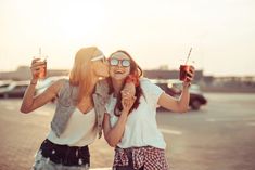 two women standing next to each other with drinks in their hands and one is kissing the other