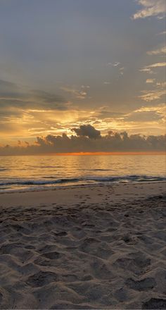 the sun is setting over the ocean with clouds in the sky and sand on the beach