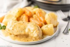 a white plate topped with potatoes and meat covered in gravy next to a pot of broccoli