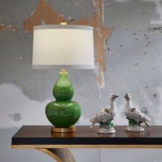 two birds on a table next to a green vase with a white lamp in the background