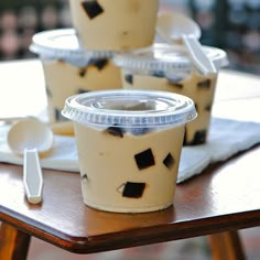 three plastic cups sitting on top of a table with spoons in front of them