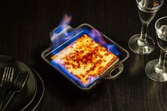 a square casserole in a pan on a table next to wine glasses