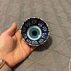 a hand holding a blue and white bowl with an evil eye on it