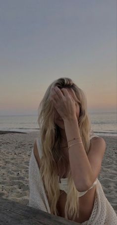 a woman sitting on top of a wooden bench next to the ocean with her head in her hands