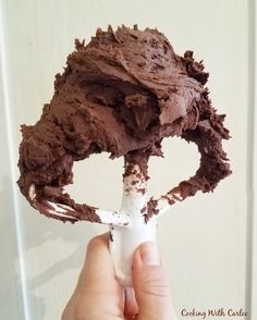 a person holding up a piece of cake with chocolate frosting on it's side