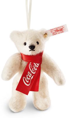 a white teddy bear with a coca - cola bottle on it's back hanging from a string